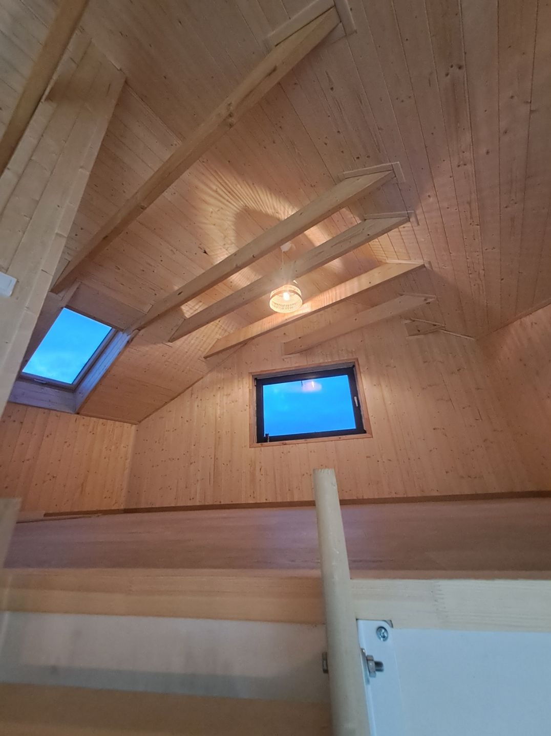 Drewniane wykończenie poddasza z widocznymi belkami stropowymi, oknem dachowym i lampą wiszącą.