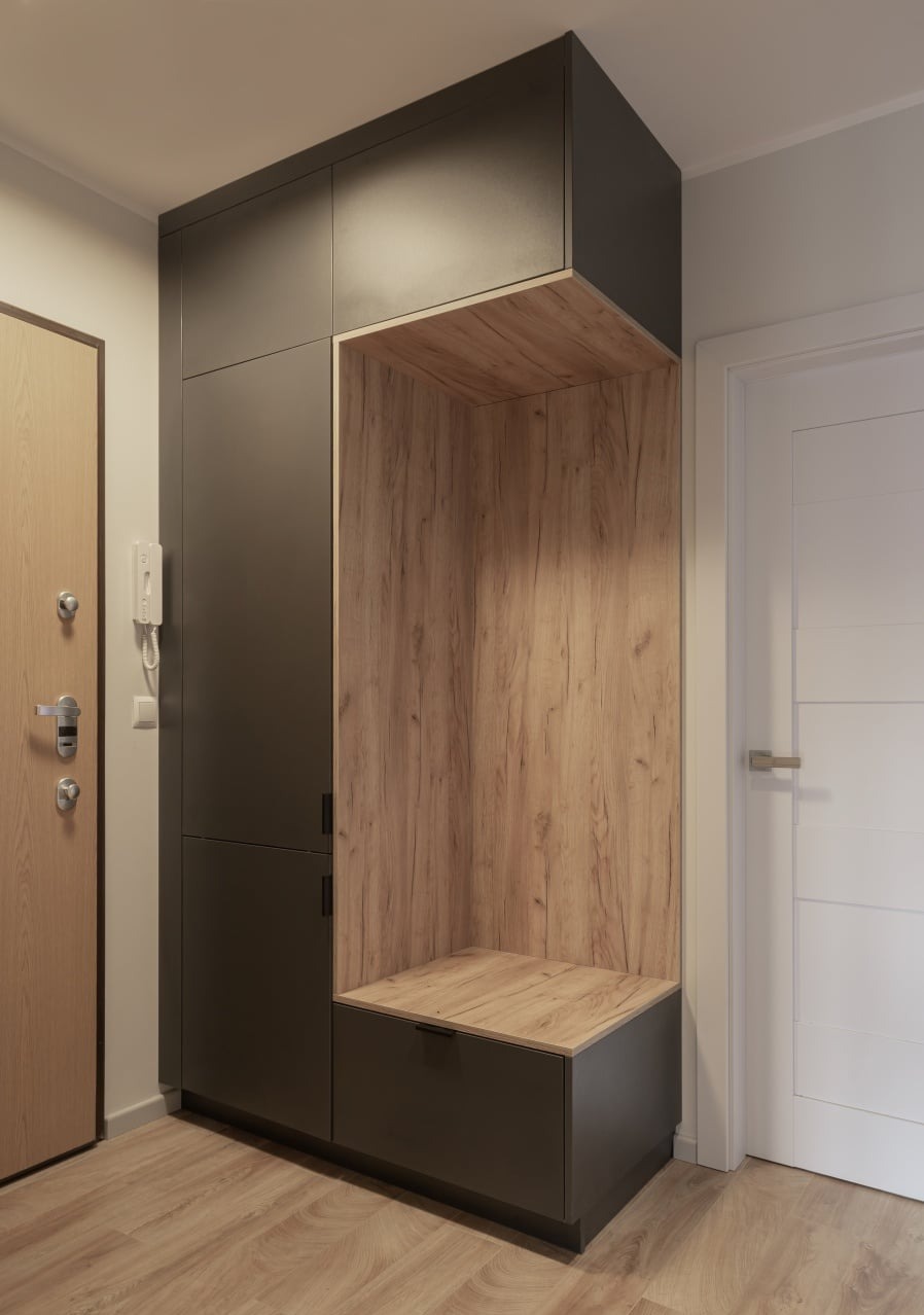 Ciemnoszara szafa wnękowa z otwartą przestrzenią z drewnianym wykończeniem i siedziskiem w przedpokoju.