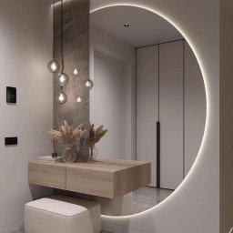 Banasiak kompleksowe wykończenia wnętrz - Nowoczesna aranżacja przedpokoju z okrągłym lustrem podświetlonym LED, wiszącą konsolą z drewnianym blatem, szklanymi wazonami z suszonymi trawami i pufą w kolorze ecru na marmurowej podłodze.