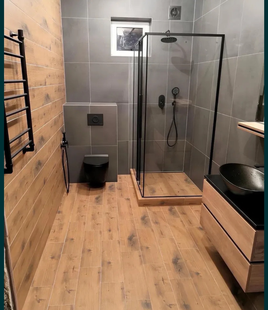 Nowoczesna łazienka z kabiną prysznicową typu walk-in z czarną ramą, umywalką nablatową w kształcie misy, drewnopodobną podłogą i szarymi płytkami ściennymi.
