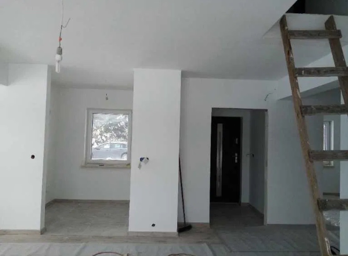 Wnętrze w trakcie malowania na biało, widoczna drabina drewniana, surowa żarówka i przygotowane podłoże.