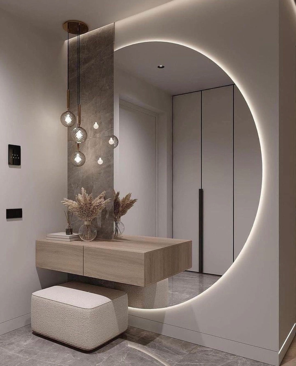 Nowoczesna aranżacja przedpokoju z okrągłym lustrem podświetlonym LED, wiszącą konsolą z drewnianym blatem, szklanymi wazonami z suszonymi trawami i pufą w kolorze ecru na marmurowej podłodze.