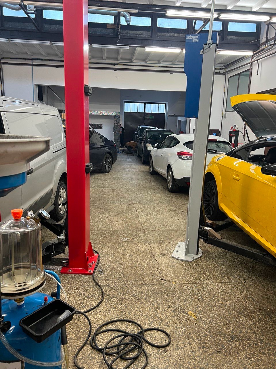 Wnętrze warsztatu samochodowego w Sopocie z kilkoma pojazdami, w tym żółtym autem na podnośniku i sprzętem diagnostycznym na pierwszym planie.