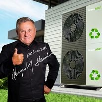 Uśmiechnięty mężczyzna w czarnej koszuli z napisem 'polecam' i odręcznym podpisem, stojący przed pompą ciepła Green AGE z dwoma wentylatorami i zielonymi symbolami recyklingu.