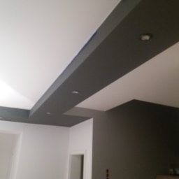 Bartosz Stec - Pomieszczenie po remoncie z pomalowanym sufitem z elementami podwieszanymi w kolorze szarym i zamontowanymi punktowymi źródłami światła