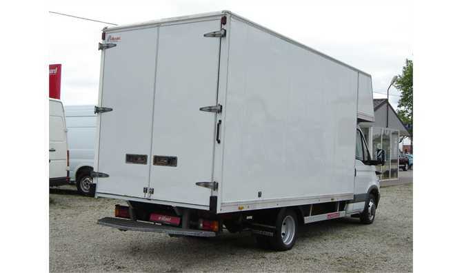 Tył białego samochodu dostawczego z zamkniętymi drzwiami kontenera, widoczny hak holowniczy i tablica rejestracyjna z czerwoną naklejką.