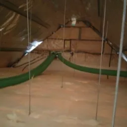 Poddasze po izolacji pianą PUR z widocznymi zielonymi rurami wentylacyjnymi i metalowymi prętami podtrzymującymi konstrukcję dachu.