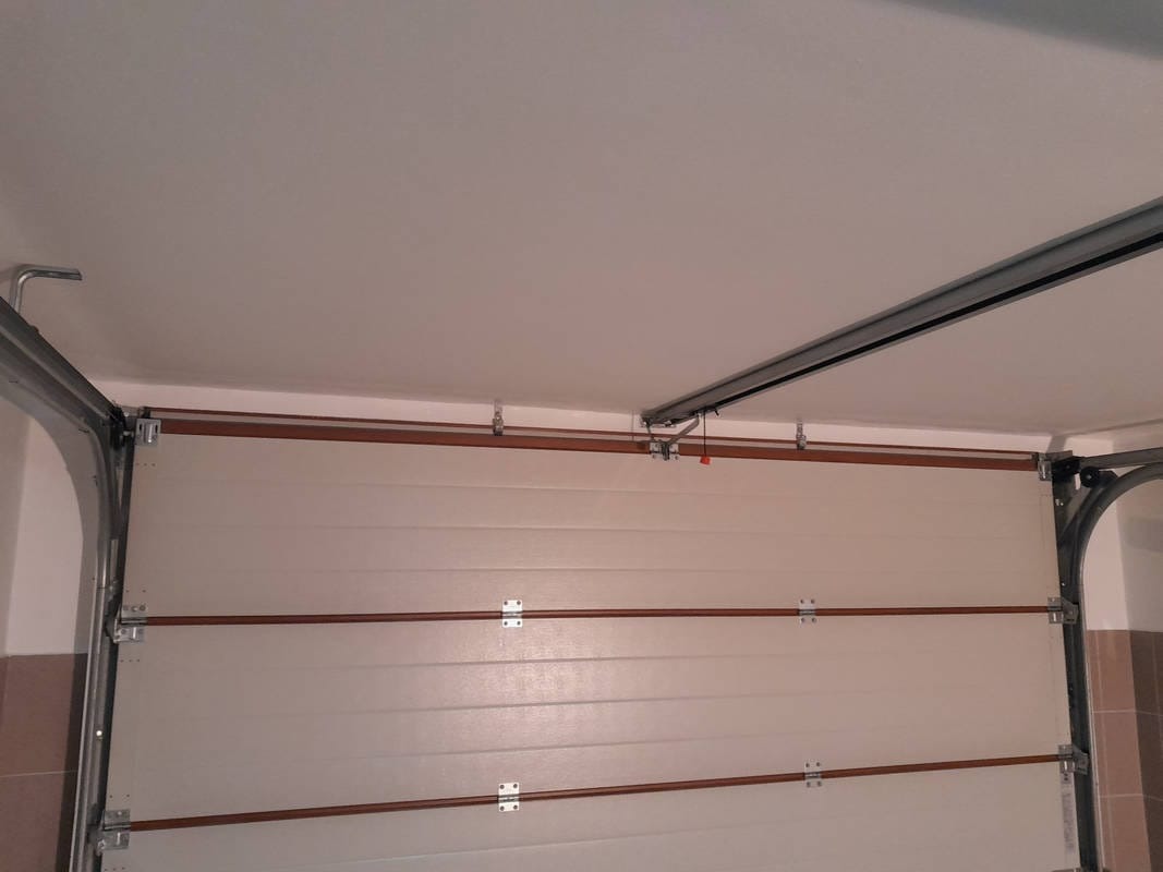 Wnętrze garażu z widoczną częściowo otwartą segmentową bramą garażową, szynami prowadzącymi i mocowaniami do sufitu.