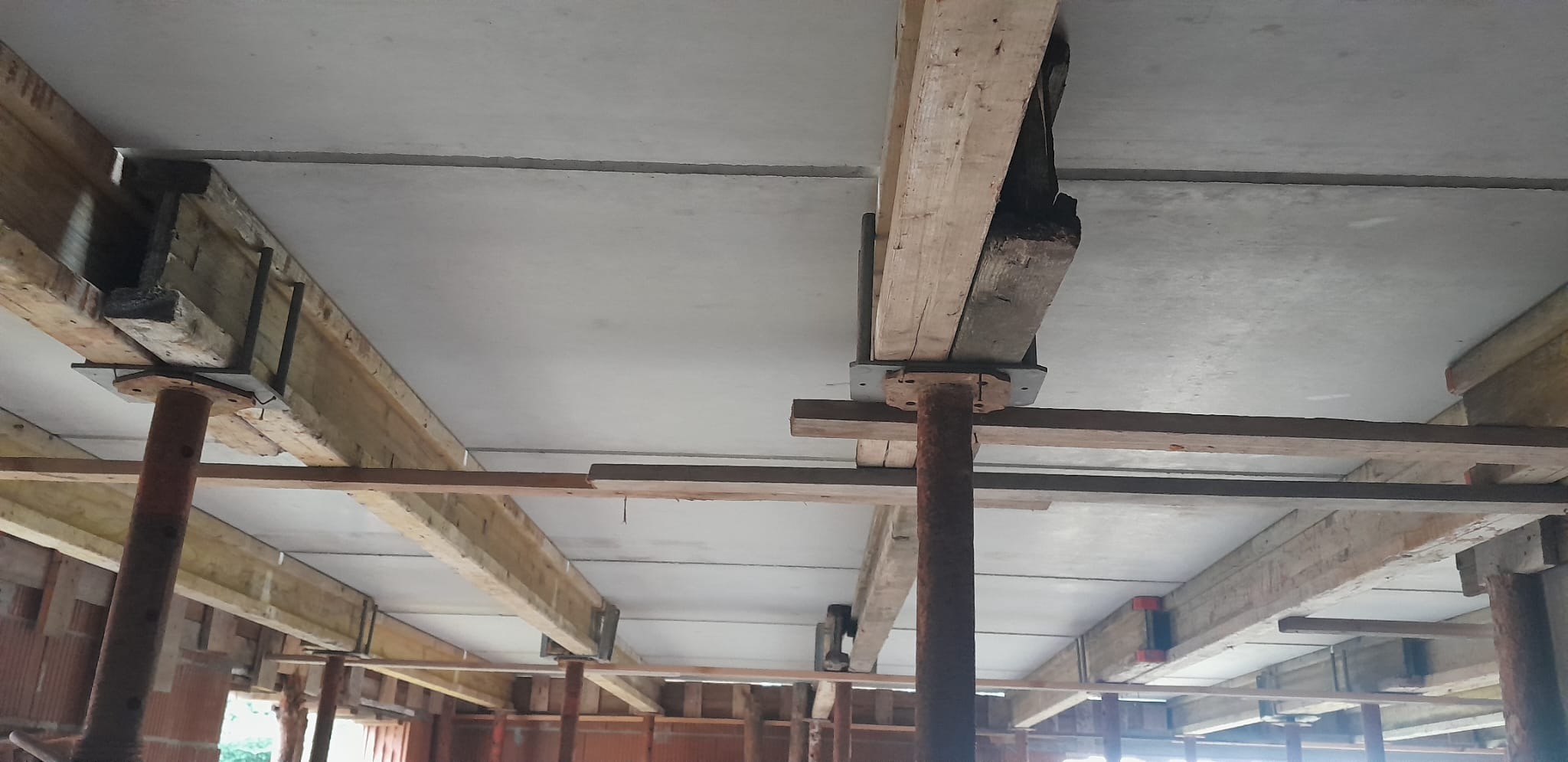 Szare płyty stropowe podparte drewnianymi belkami i metalowymi stemplami budowlanymi w trakcie prac remontowych.