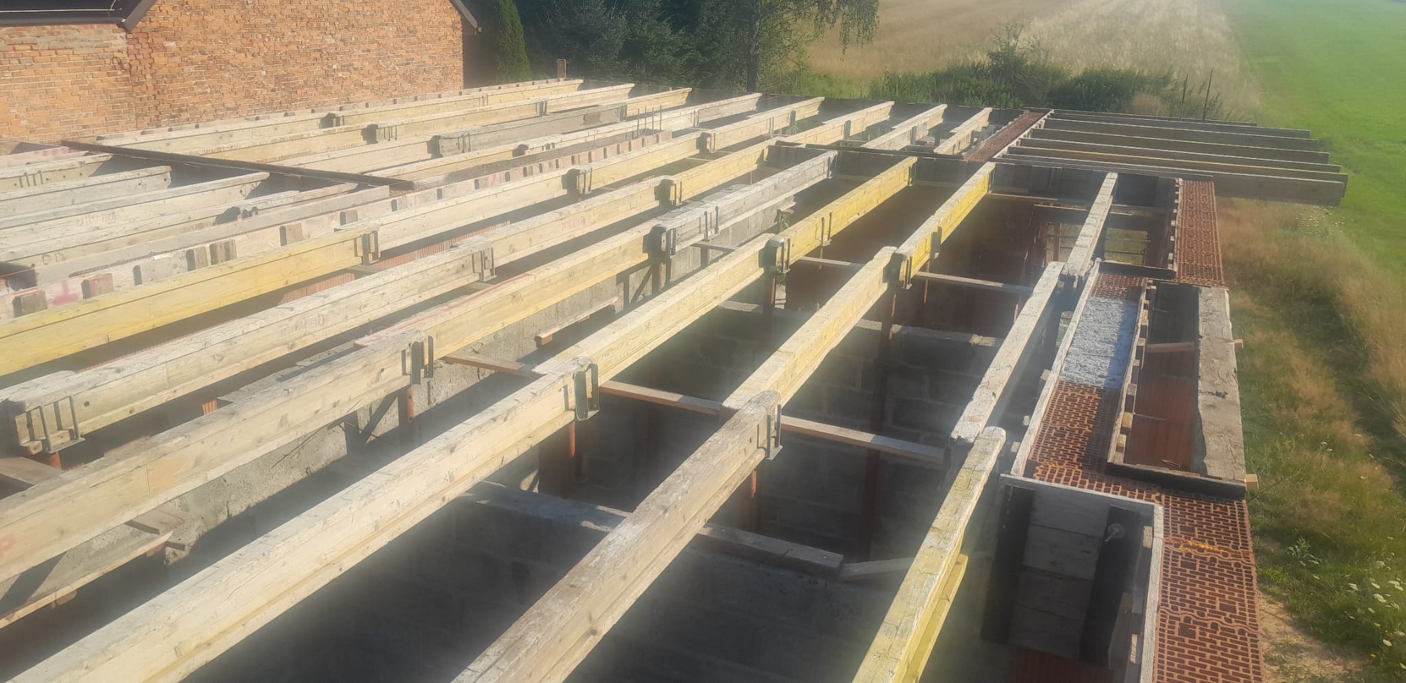 Konstrukcja stropu z drewnianych belek na betonowych ścianach, widok z góry na budowę w trakcie realizacji.