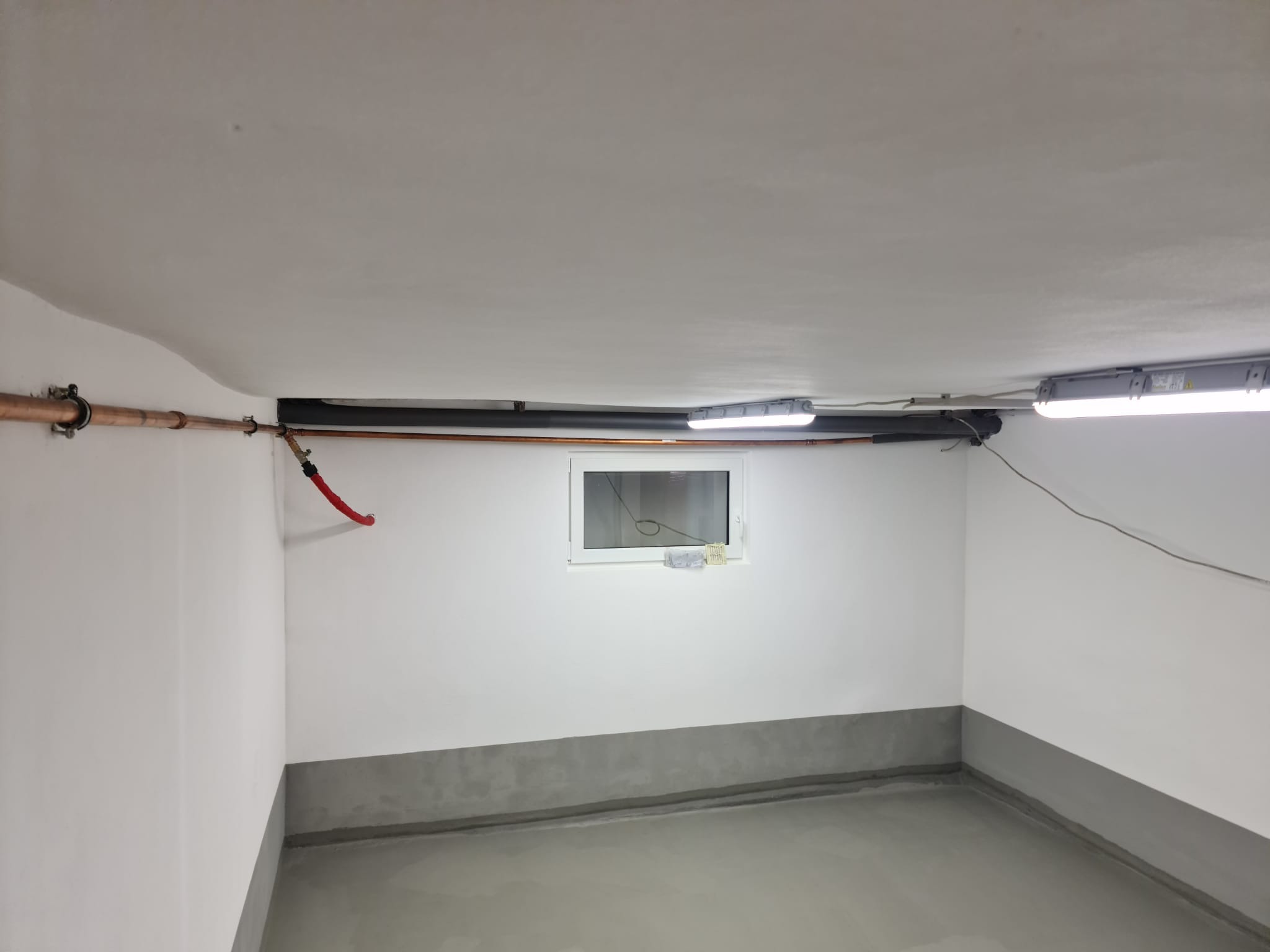 Wnętrze piwnicy w Miasteczku Śląskim po wylewce, z widocznymi instalacjami pod sufitem i oknem.