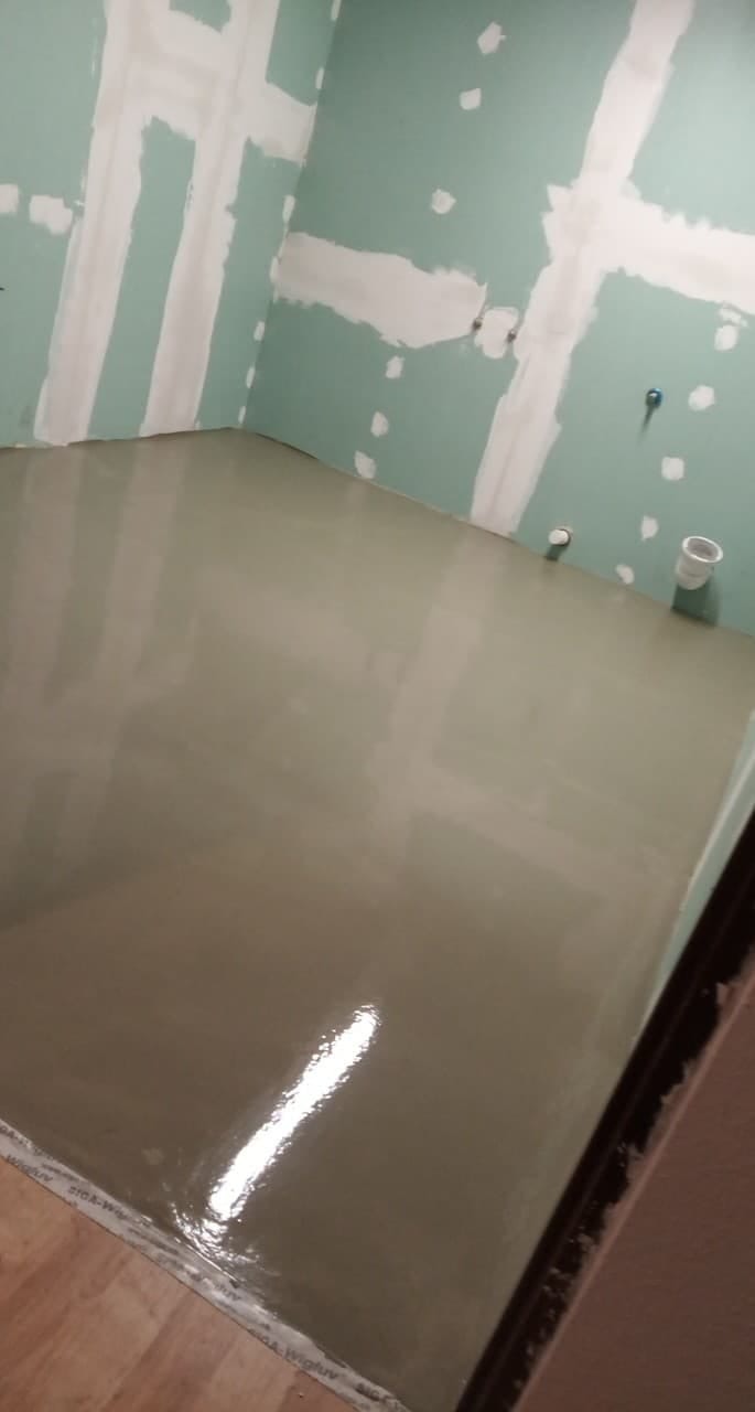 Świeżo wylana, samopoziomująca wylewka na podłodze w pomieszczeniu z przygotowanymi ścianami do malowania, widoczne ślady po szpachlowaniu