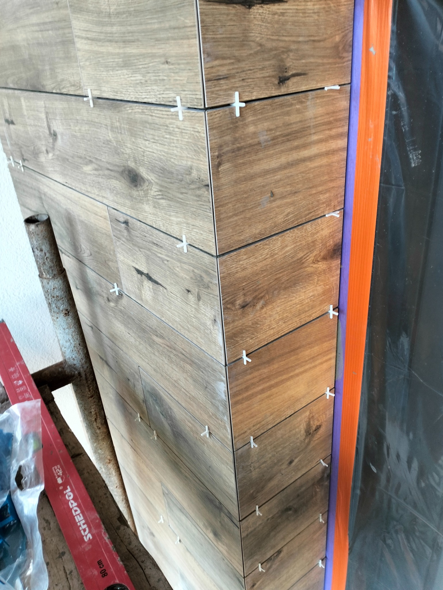 Płytki imitujące drewno, ułożone na ścianie z użyciem krzyżyków dystansowych, widoczna listwa krawędziowa i poziomica.