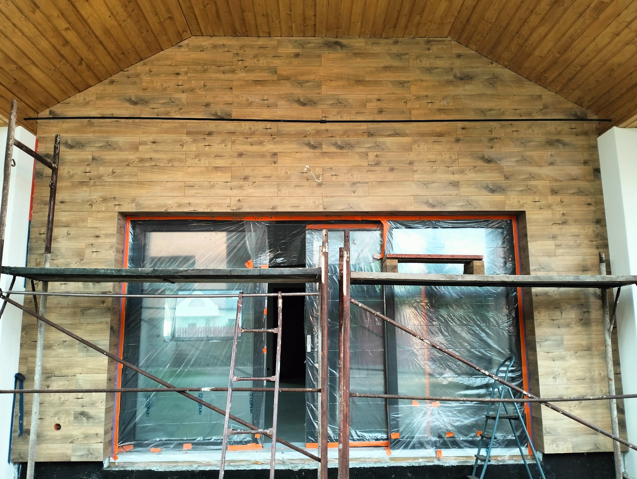 Montaż płytek imitujących drewno na elewacji budynku, widoczne rusztowanie i folia ochronna na oknach.