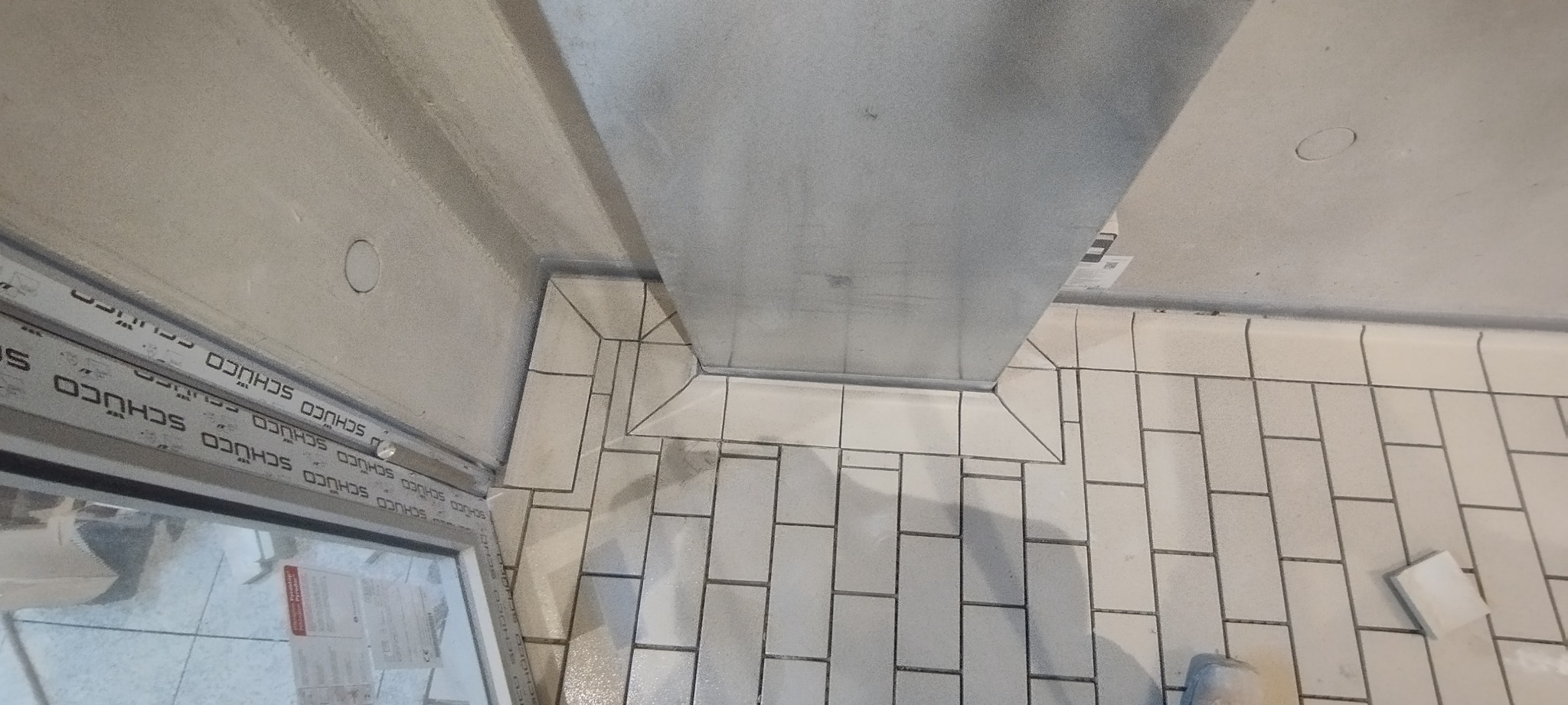 Ułożone białe, prostokątne płytki podłogowe w łazience w Dębnie, widok z góry, z widocznym odpływem liniowym i oknem z profilem SCHÜCO.