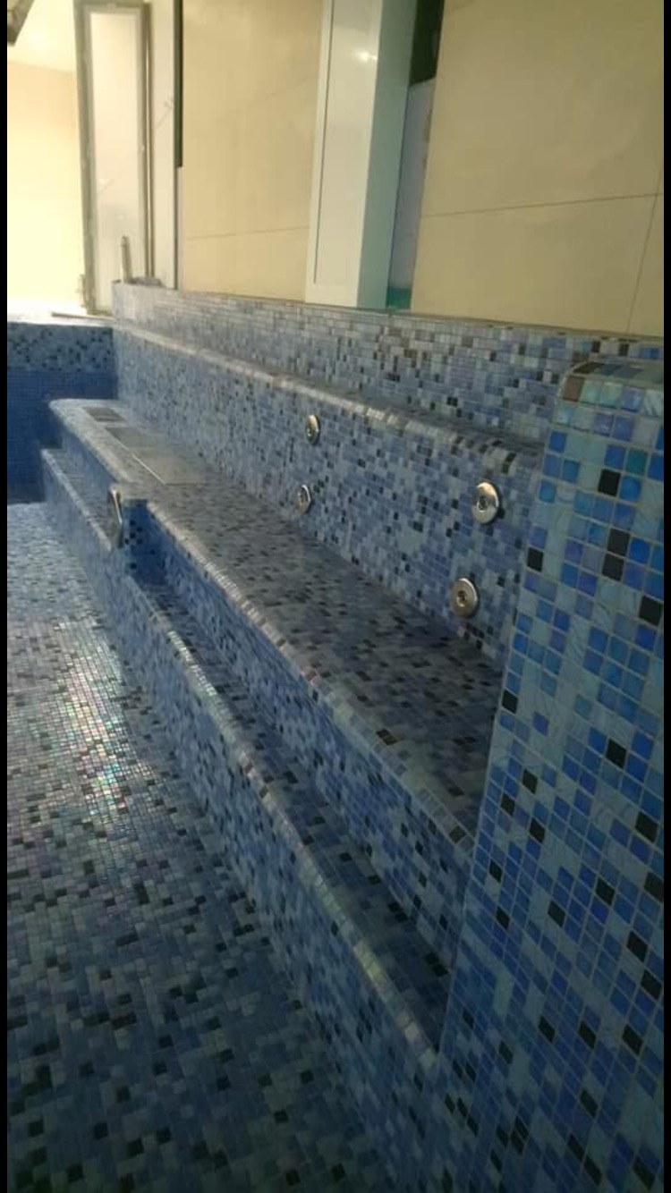 Wykończone schody do basenu z mozaiką w odcieniach błękitu i szarości, z dyszami hydromasażu.