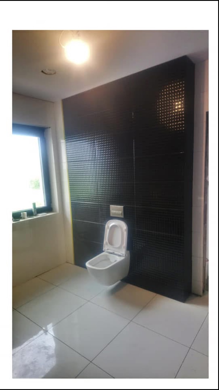 Nowoczesna łazienka z wiszącą toaletą na tle ściany wyłożonej czarnymi płytkami z delikatnym wzorem, białe płytki podłogowe, okno z widokiem na zewnątrz, oświetlenie sufitowe