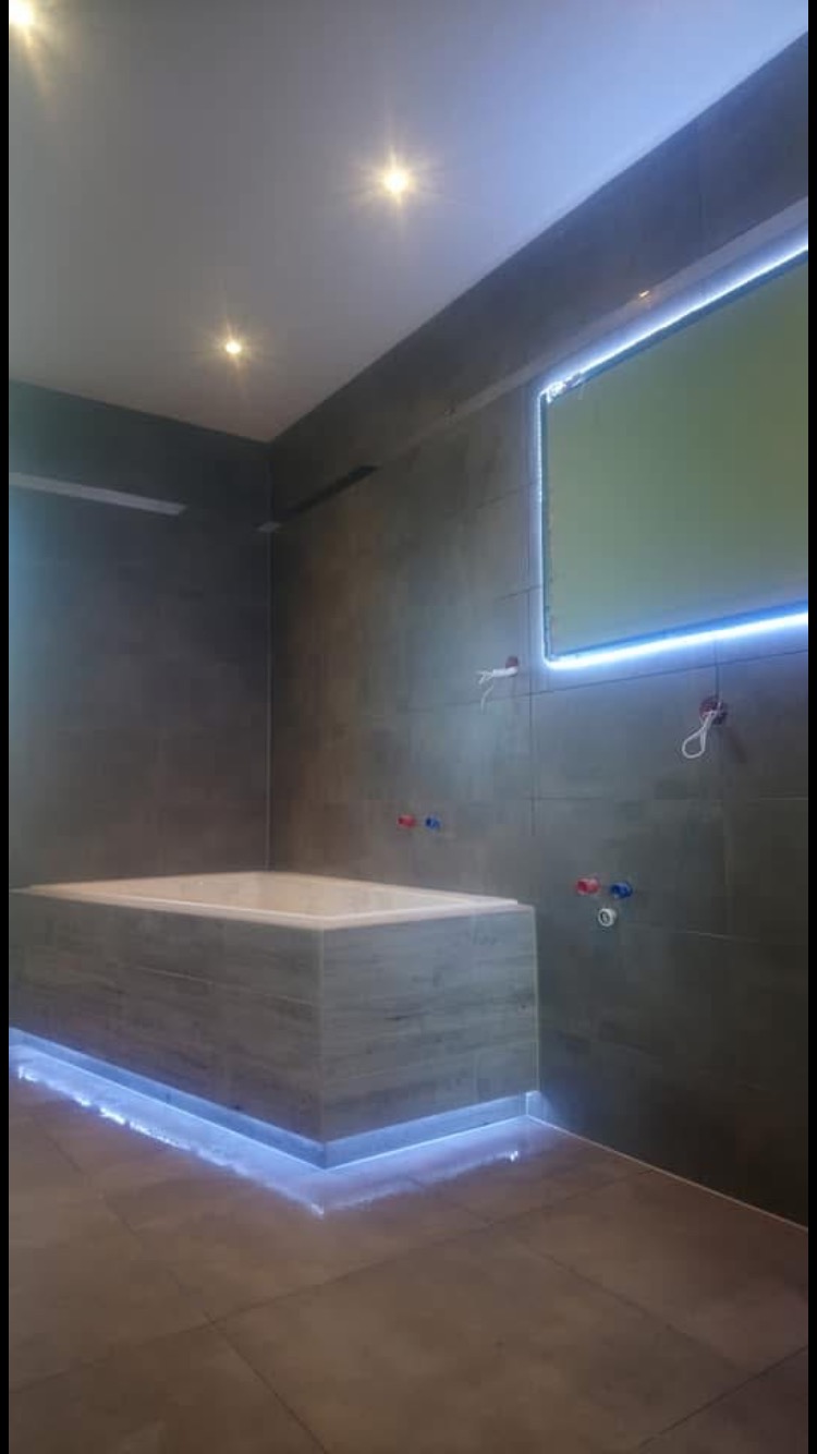 Nowoczesna łazienka w Ostrowie Wielkopolskim z podświetlaną wanną obudowaną płytkami imitującymi beton, szare płytki na ścianach i podłodze, oraz podświetlone lustro.