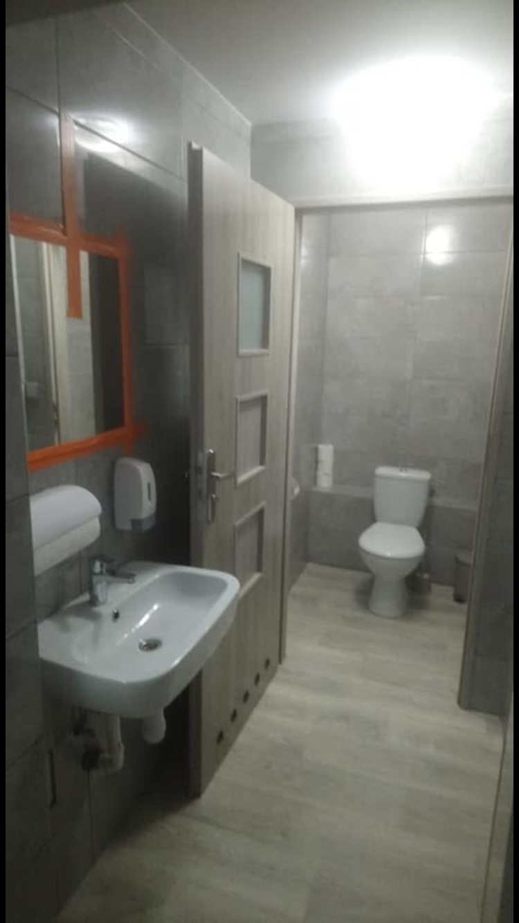 Wyremontowana łazienka w szarościach z umywalką, toaletą i drewnopodobną podłogą, widoczne akcesoria łazienkowe.