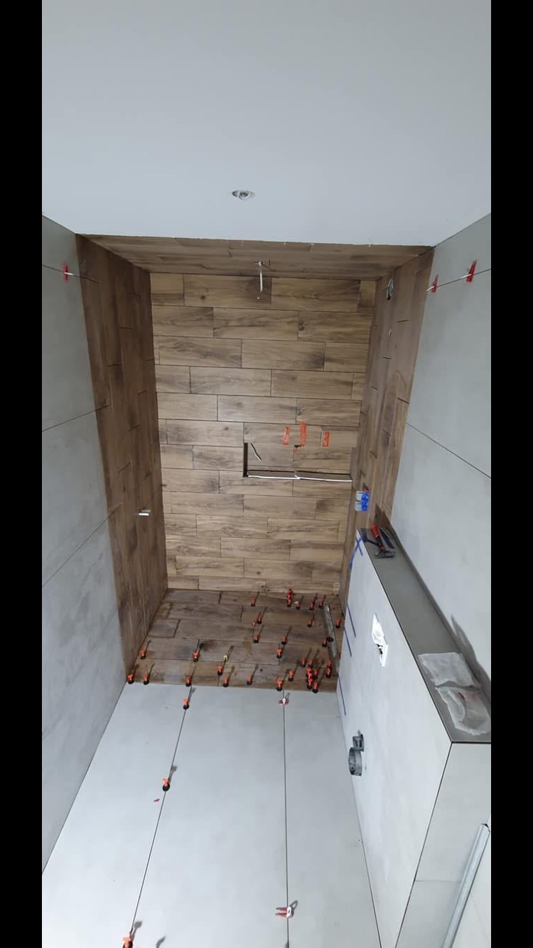 Montaż płytek imitujących drewno na ścianie w łazience, widoczne krzyżyki dystansowe, poziomica i przewody pomiarowe.