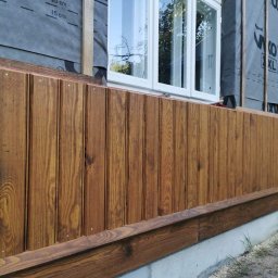 DC Remonty Daniel Czajkowski - Fragment elewacji budynku z drewnianą boazerią w kolorze brązowym, widoczna izolacja przeciwwilgociowa i białe okno.