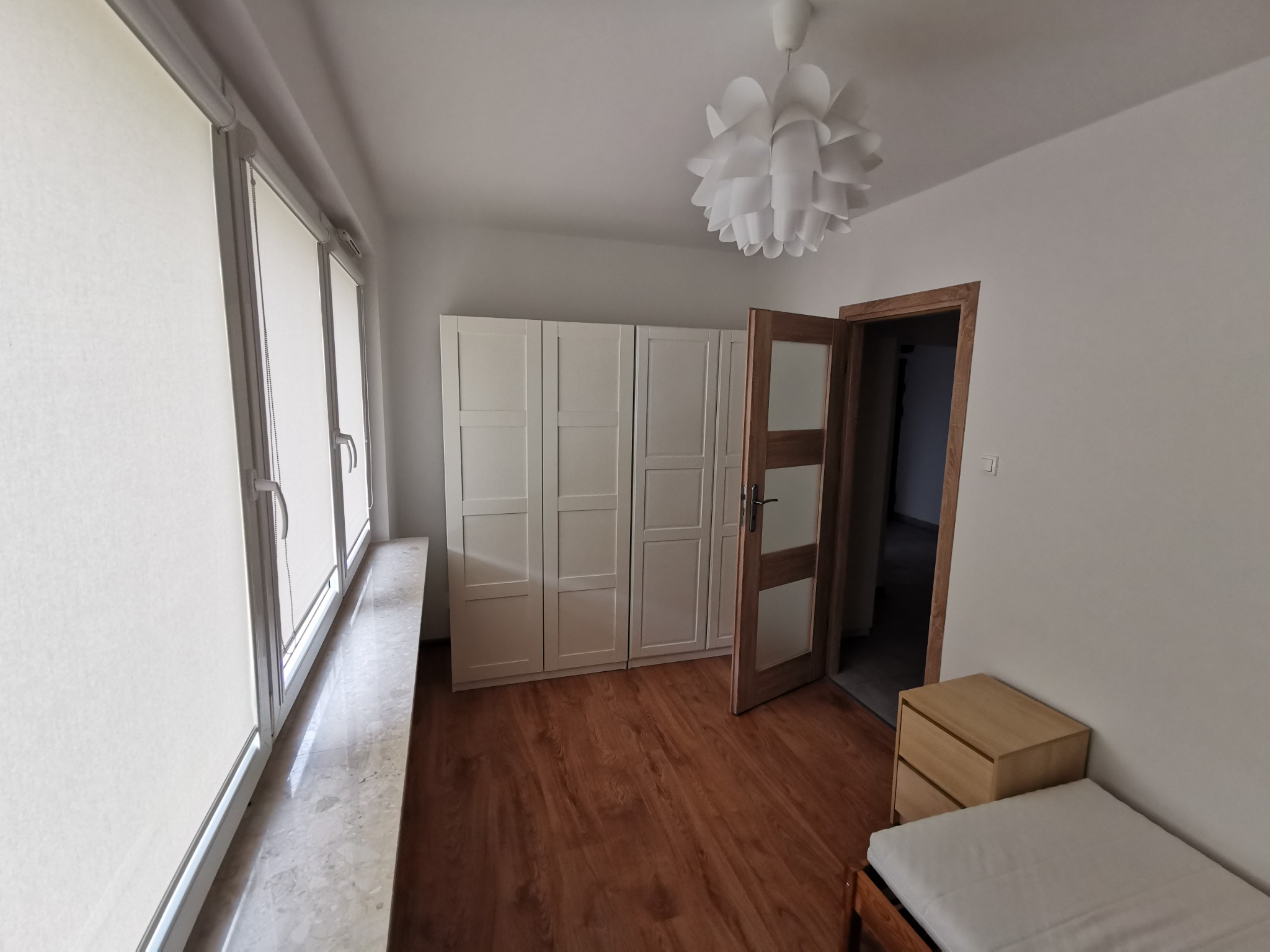 Jasne wnętrze pokoju w Sokołach po odświeżeniu ścian, z widocznymi roletami okiennymi, białymi szafami w zabudowie i drewnianą podłogą.