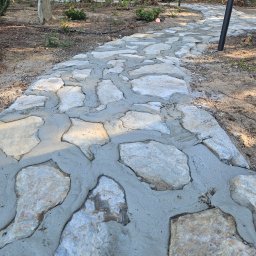 Green Dream Natalia Malczyk - Ścieżka ogrodowa z nieregularnych kamieni, świeżo połączonych zaprawą cementową, prowadząca przez leśny teren z młodymi drzewami i lampami ogrodowymi.