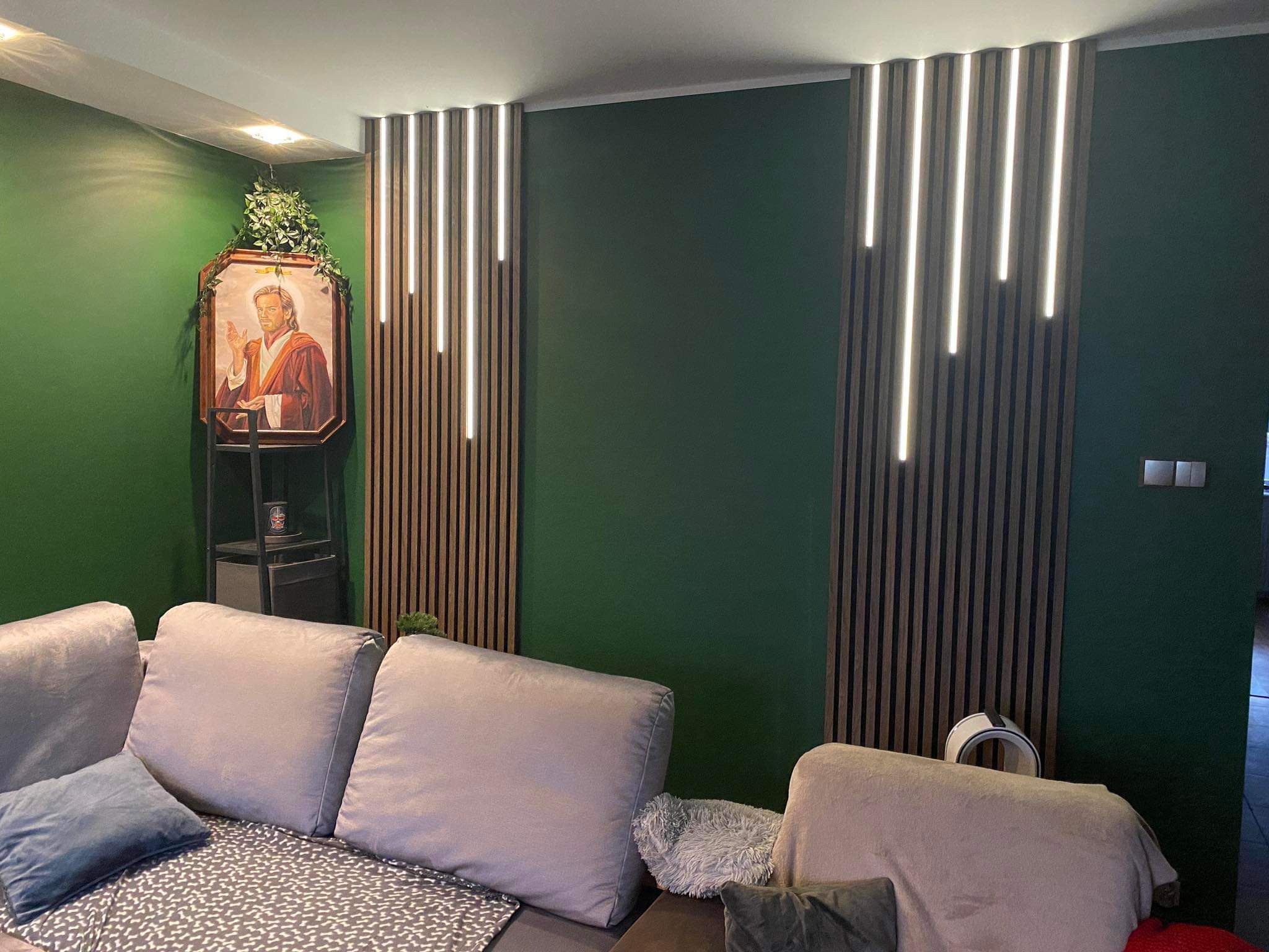 Salon z zieloną ścianą, drewnianymi lamelami z oświetleniem LED i obrazem w ramie. Nowoczesny design wnętrza z szarą sofą i dekoracjami.
