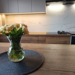 Meble na wymiar - Karol Światłoń - Nowoczesna kuchnia z szarymi szafkami górnymi i drewnianymi dolnymi, oświetlenie LED podszafkowe, marmurowy backsplash, bukiet kremowych róż w szklanym wazonie na drewnianym blacie.