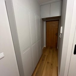 Meble na wymiar - Karol Światłoń - Szara szafa wnękowa z górnymi szafkami w przedpokoju, drewniana podłoga, widok na drzwi wejściowe.
