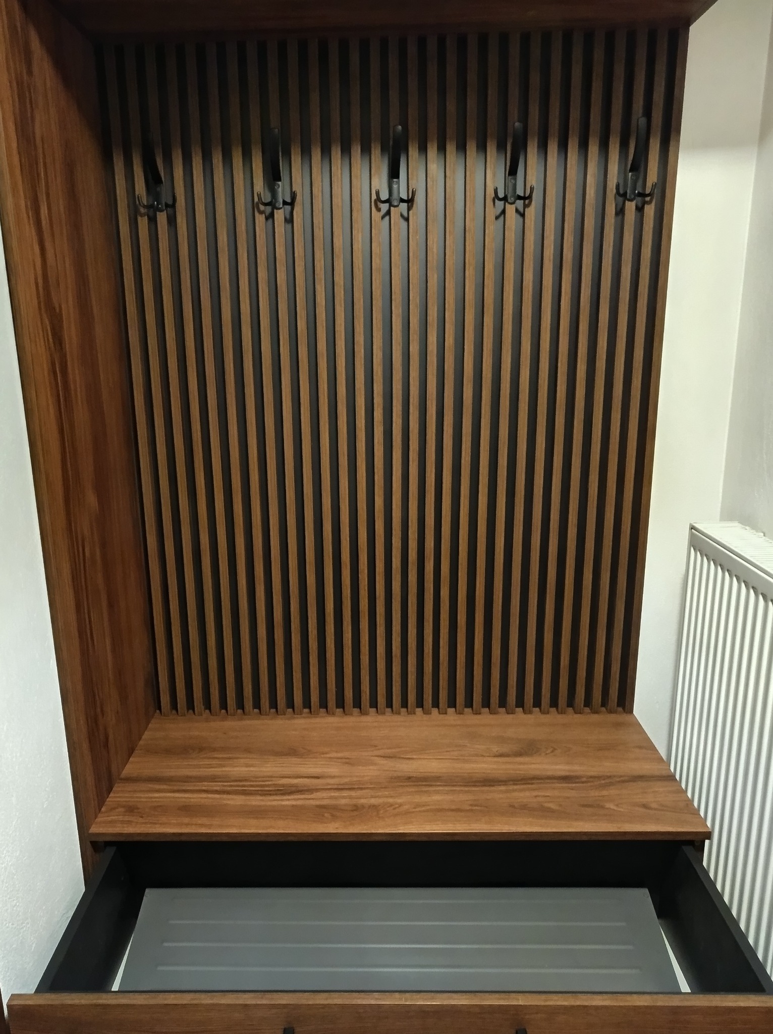 Drewniana szafa wnękowa z otwartą szufladą i wieszakami na ubrania, pionowe listwy dekoracyjne na tylnej ściance.