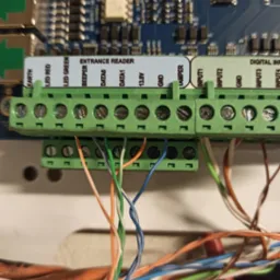 Szczegółowe ujęcie z bliska podłączenia przewodów do zielonych listew zaciskowych na płytce elektronicznej Entrance Reader z widocznymi opisami wejść/wyjść
