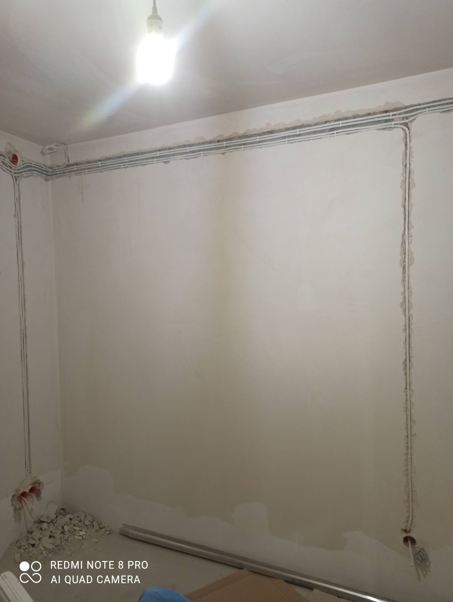 Szare korytka kablowe ułożone pod sufitem w surowym stanie, z widocznymi przewodami w ścianie i gruzem po kuciu pod gniazdka.