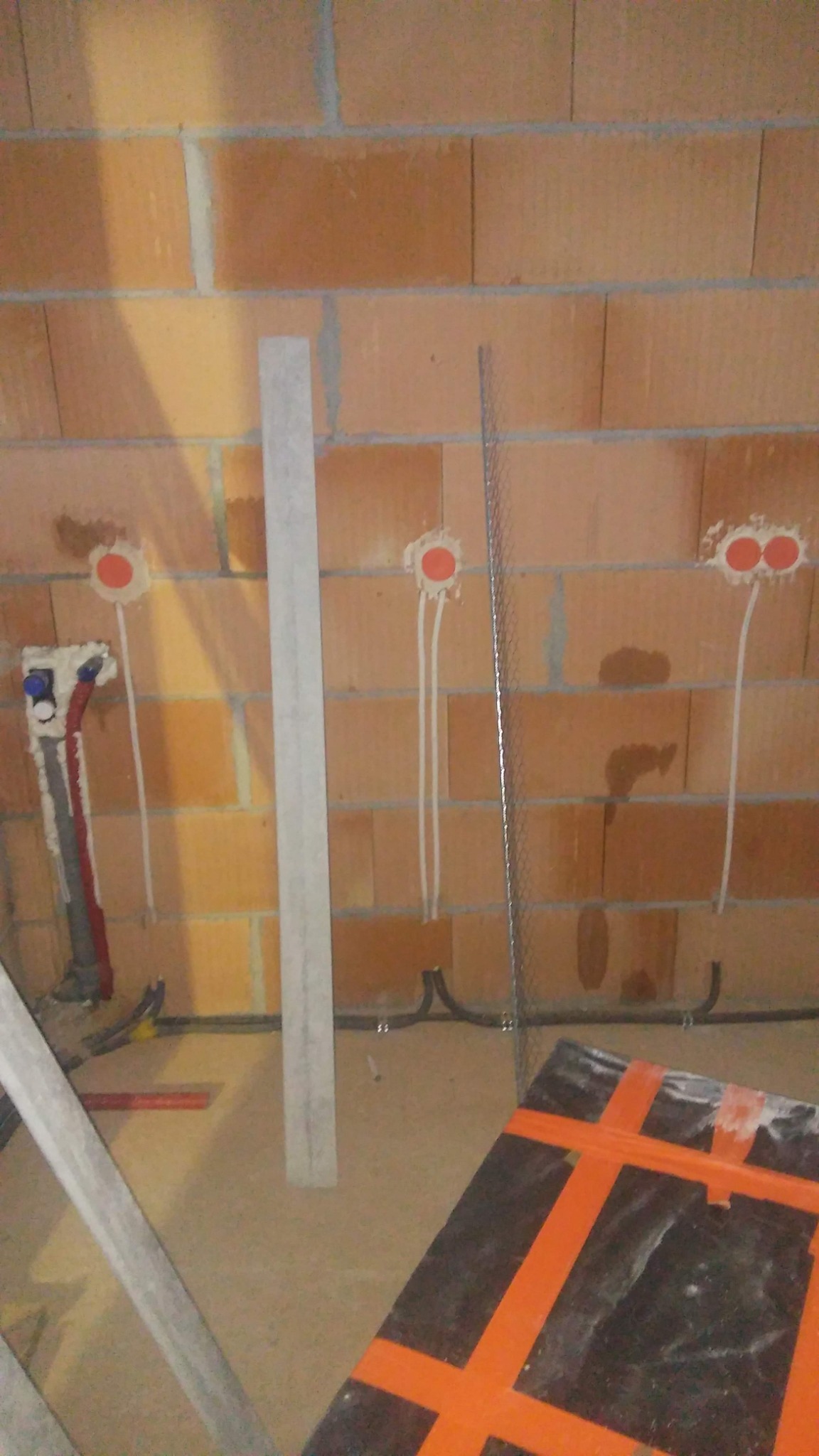 Surowa ściana z cegły z puszkami instalacyjnymi, wystającymi przewodami elektrycznymi, rurami wodnymi i elementami konstrukcyjnymi podłoża w trakcie prac wykończeniowych.