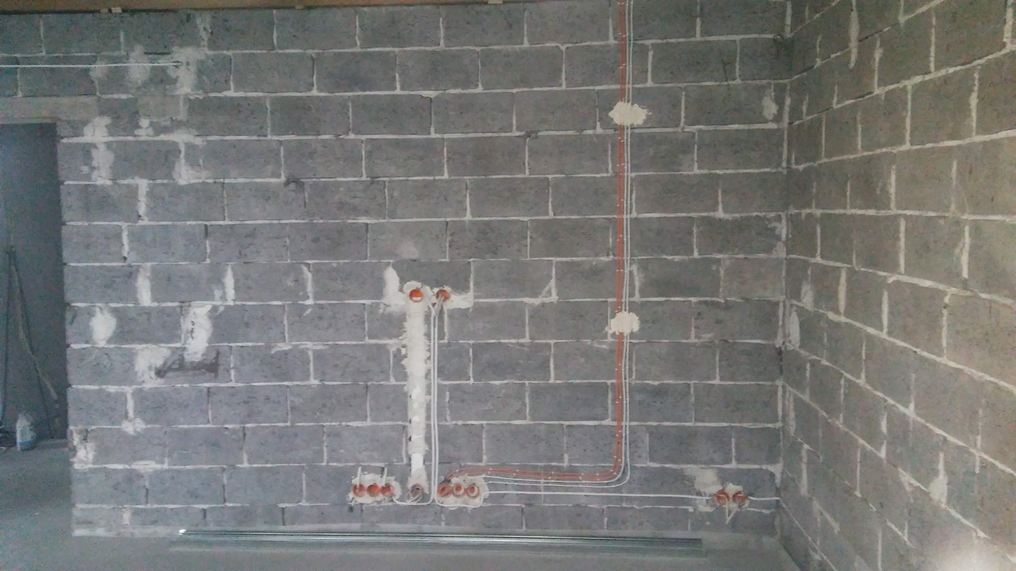 Surowa ściana z betonu komórkowego z widocznymi przewodami elektrycznymi, puszkami instalacyjnymi i częściowo nałożoną zaprawą gipsową.