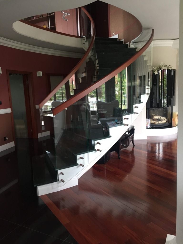 Eleganckie spiralne schody z ciemnego drewna i szklanymi balustradami w przestronnym wnętrzu z parkietem.