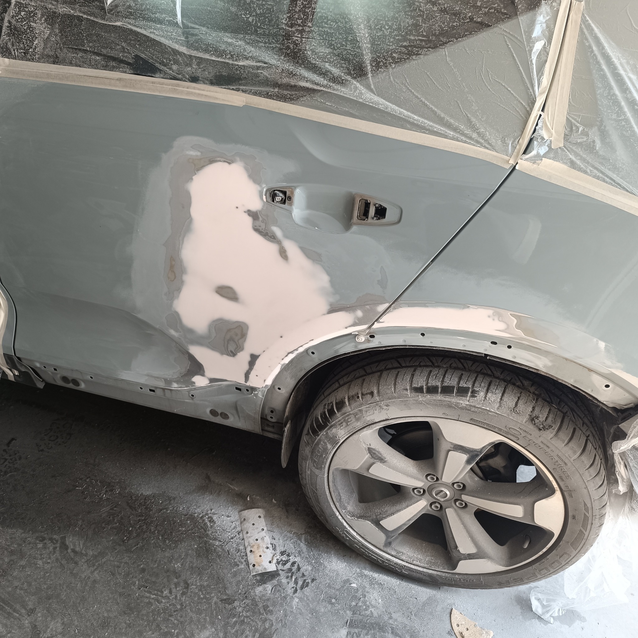 Przygotowanie powierzchni bocznej karoserii samochodu do lakierowania; widoczna nałożona szpachla, zabezpieczenie folią i taśmą malarską.