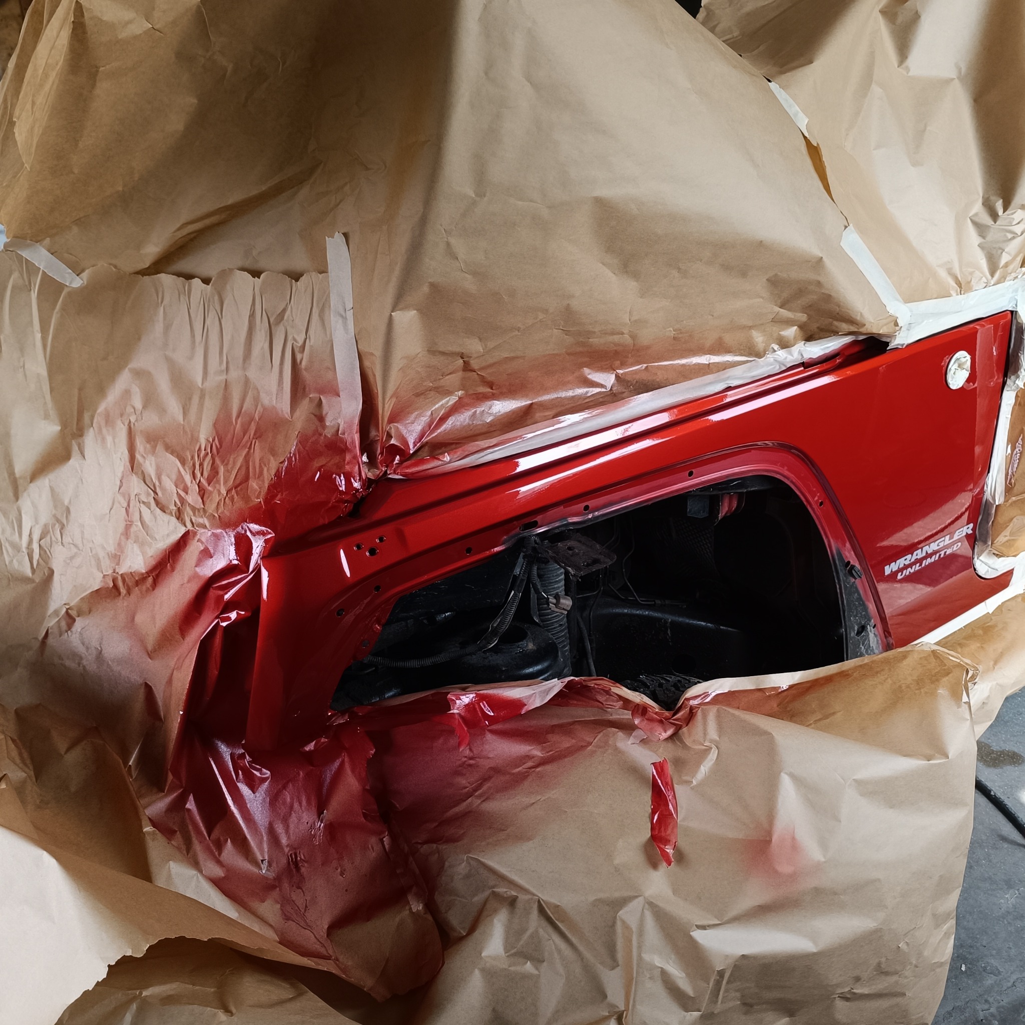 Czerwony element karoserii Jeep Wrangler Unlimited, świeżo po lakierowaniu, zabezpieczony papierem maskującym i taśmą malarską.