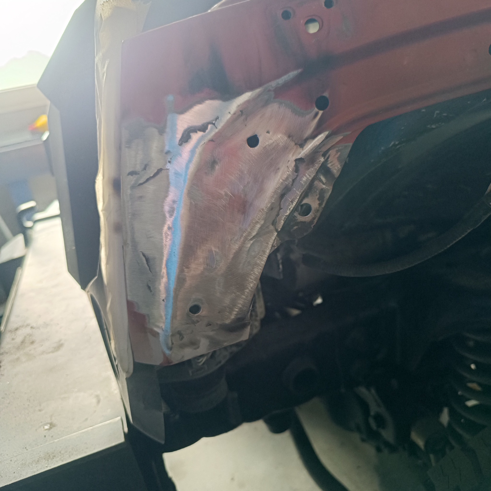 Fragment nadkola samochodu w trakcie naprawy, z widocznymi śladami szlifowania i spawania blachy, przygotowany do dalszych prac lakierniczych.