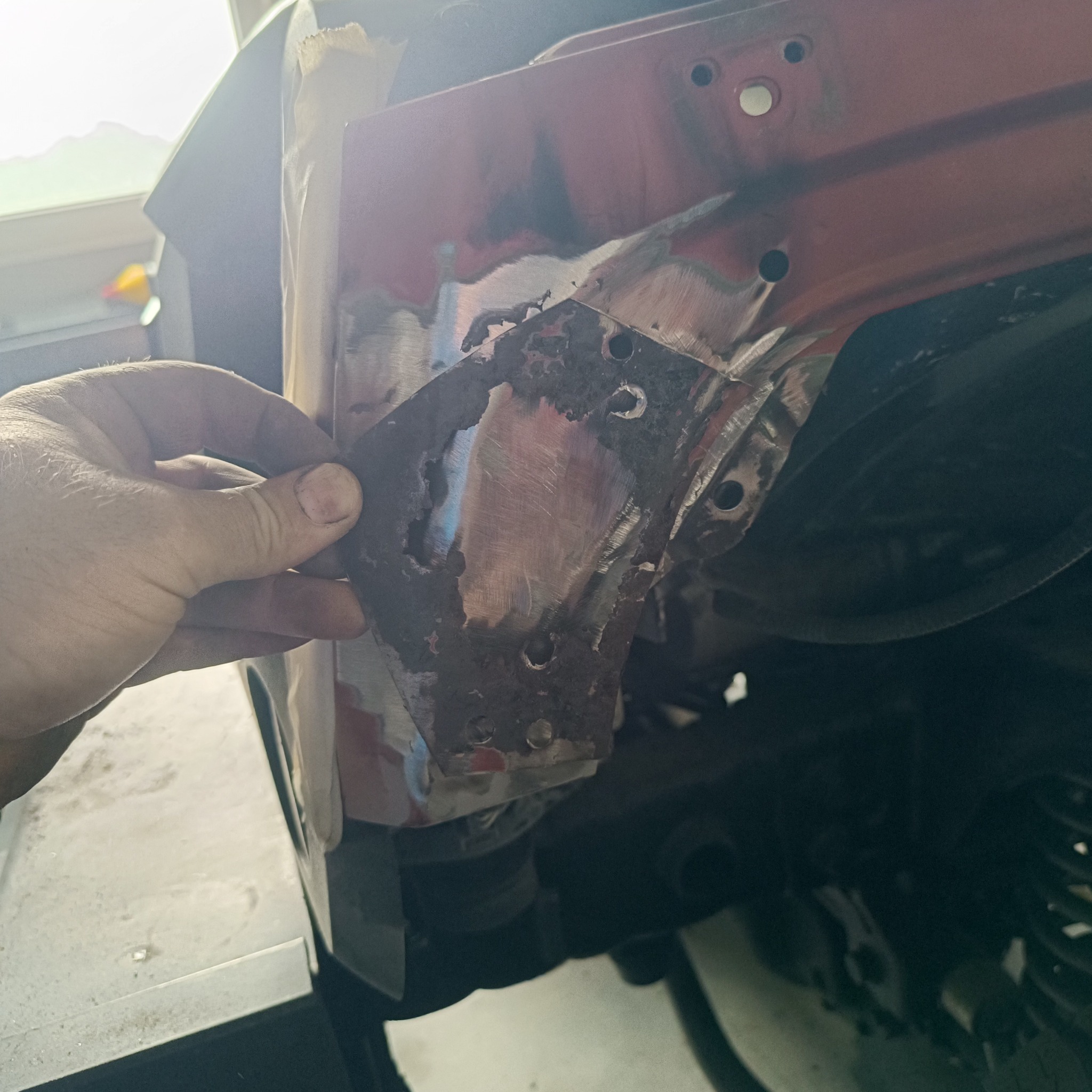 Fragment nadkola samochodu w trakcie naprawy blacharskiej, z widocznymi śladami korozji i nowo wspawanym elementem, trzymanym w dłoni.