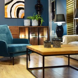 Drewbetex - Salon z turkusowym fotelem klubowym, drewnianym blatem stolika kawowego na metalowej podstawie, drewnianą komodą z oświetleniem i dekoracjami.