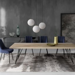 Drewbetex - Jadalnia w odcieniach szarości i granatu: stół z blatem z jasnego drewna na czarnych, metalowych nogach, otoczony granatowymi krzesłami, na wzorzystym dywanie, oświetlony trzema białymi, kulistymi...