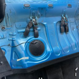 Scars Detailing - Wnętrze samochodu zdemontowane do czyszczenia, widoczne niebieskie elementy karoserii, czarne pasy bezpieczeństwa, przewody, oraz fragmenty czarnej tapicerki podłogi i tunelu środkowego.