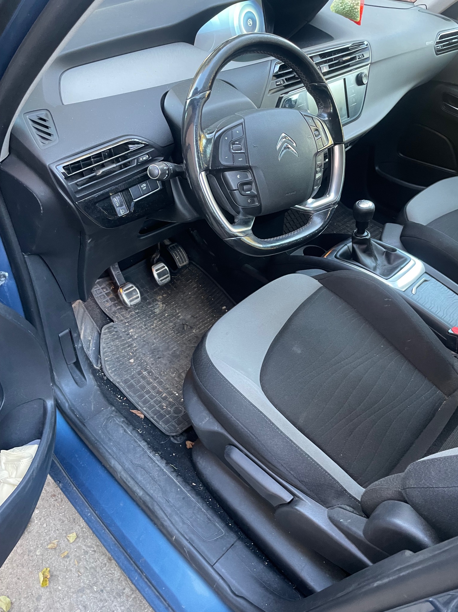 Wnętrze samochodu Citroen z widocznymi pedałami z nakładkami, brudną wycieraczką i dwukolorową tapicerką foteli, uchwycone z otwartymi drzwiami.