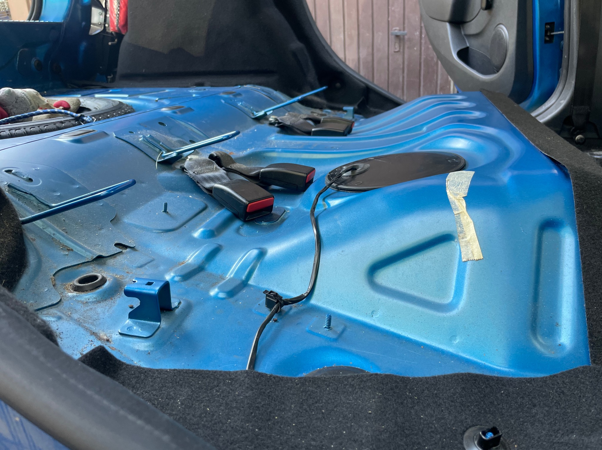 Wnętrze samochodu zdemontowane do czyszczenia, widoczne niebieskie blachy podłogowe, pasy bezpieczeństwa i elementy instalacji elektrycznej.