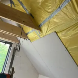 Poddasze w trakcie adaptacji: ocieplenie folią, montaż płyty karton-gips na skosach, widoczna drabina i narzędzia. Prace wykończeniowe w toku.