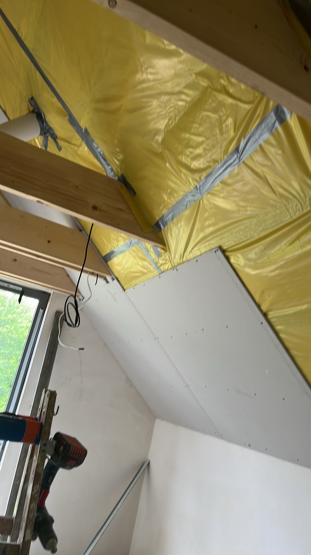 Poddasze w trakcie adaptacji: ocieplenie folią, montaż płyty karton-gips na skosach, widoczna drabina i narzędzia. Prace wykończeniowe w toku.