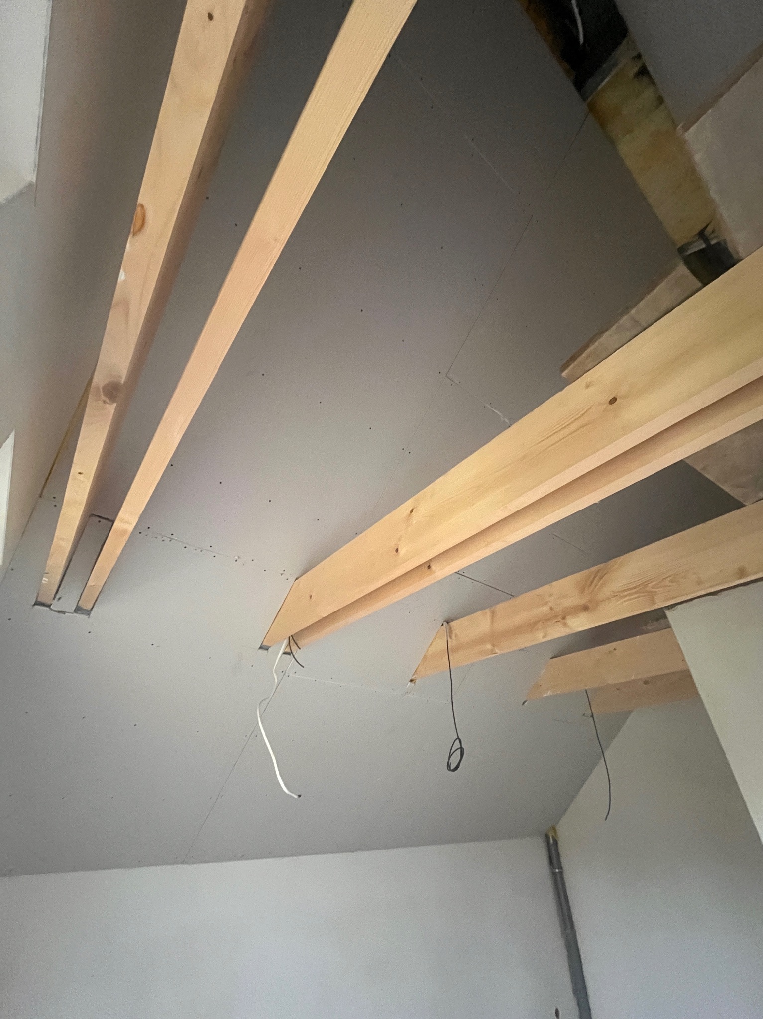 Sufit poddasza z płyt kartonowo-gipsowych i drewnianą konstrukcją nośną. Widoczne przewody elektryczne. Ujęcie z dołu, surowy stan wykończenia.