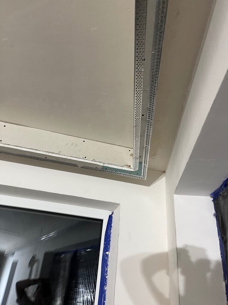 Montaż płyty KG na suficie z widocznymi profilami, narożnikami i oknem w tle. Etap wykończenia wnętrza, przygotowanie do dalszych prac.