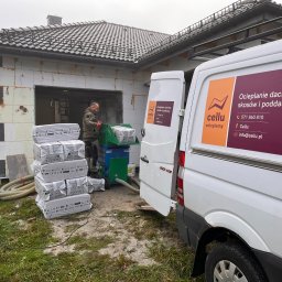 Cellu - Marcin Korzyński - Pracownik w trakcie ocieplania ścian budynku z użyciem maszyny i materiałów izolacyjnych IsoCell, obok zaparkowany biały bus z reklamą firmy Cellu.